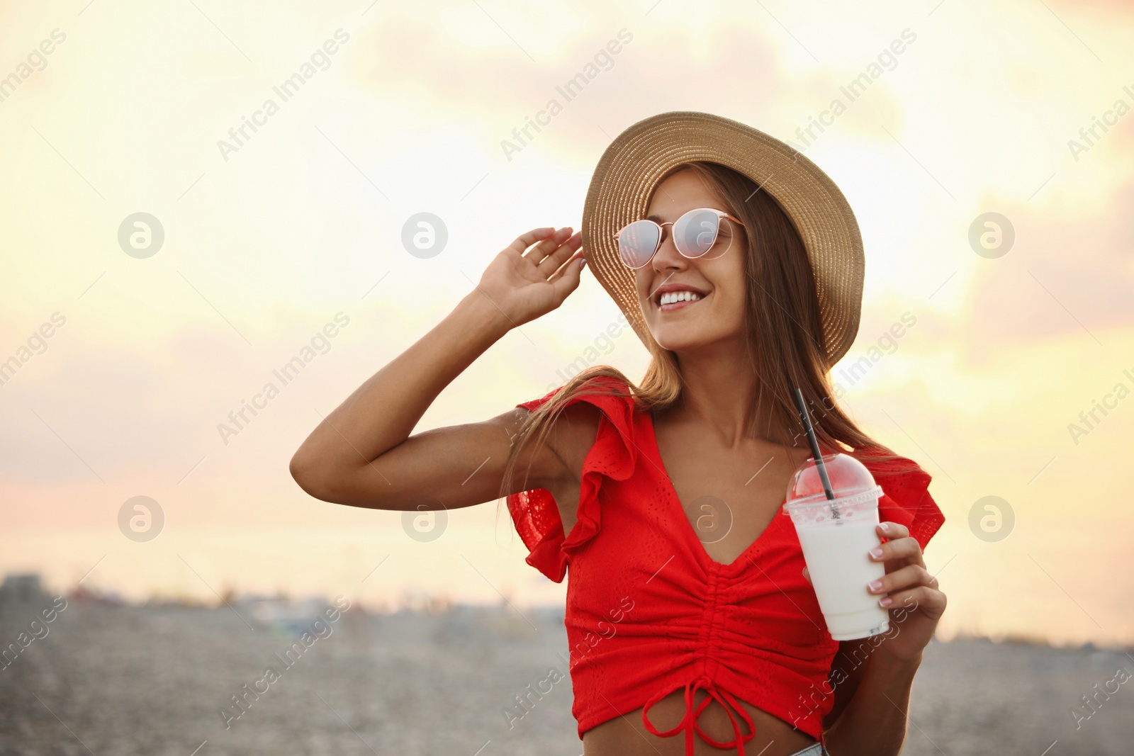 Photo of Beautiful young woman with tasty milk shake outdoors, space for text