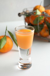 Photo of Tasty tangerine liqueur in shot glass and fresh fruits on white table