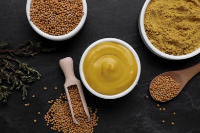 Photo of Delicious mustard, seeds and powder on black textured table, flat lay