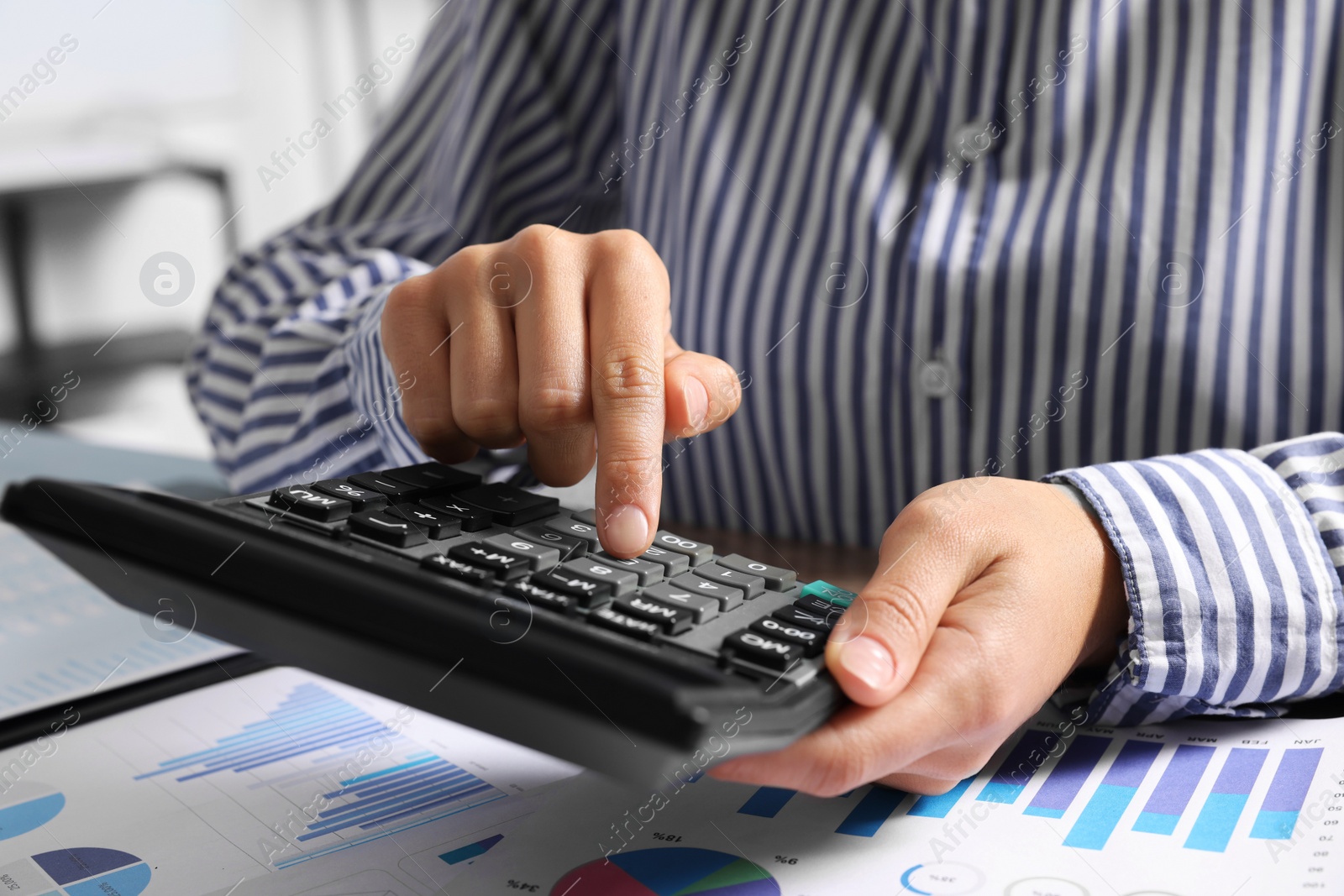 Photo of Woman using calculator at table indoors, closeup