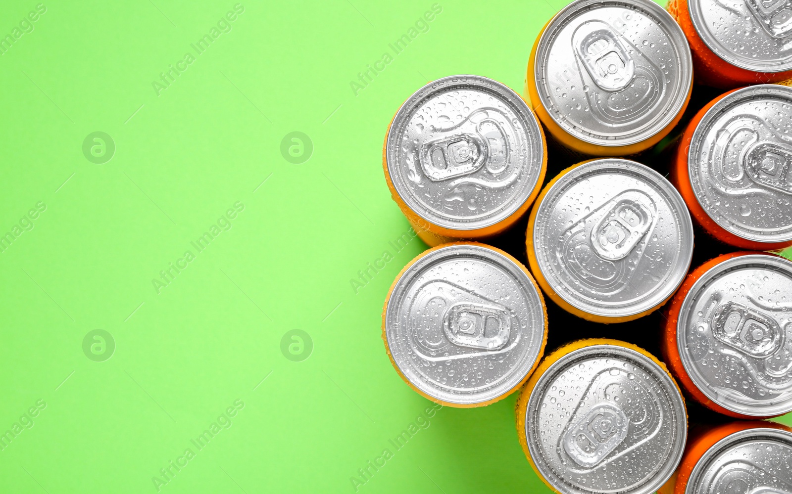 Photo of Energy drinks in wet cans on green background, top view. Space for text