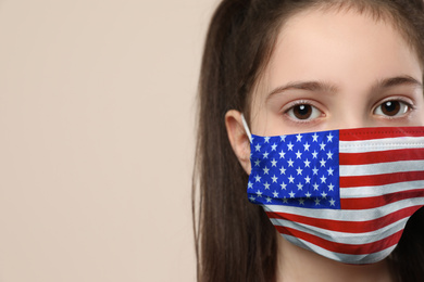 Image of Little girl wearing mask with USA flag pattern on beige background, closeup. Dangerous virus