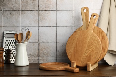 Photo of Wooden cutting boards and kitchen utensils on table near tiled wall