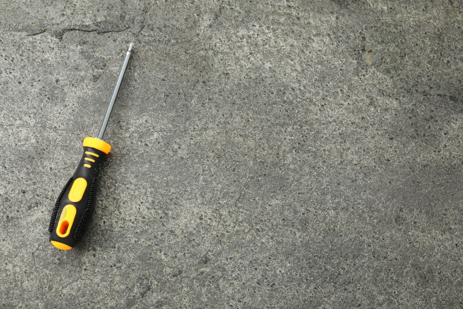 Photo of Screwdriver with black handle on grey textured table, top view. Space for text