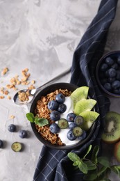 Tasty granola with yogurt, blueberries and kiwi in bowl on gray textured table, flat lay