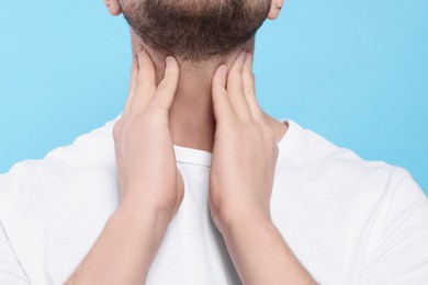 Photo of Man suffering from sore throat on light blue background, closeup