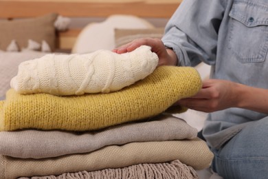 Photo of Woman with stack of different folded blankets and clothes on bed, closeup. Home textile