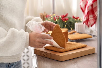 Woman making gingerbread house at wooden table, closeup