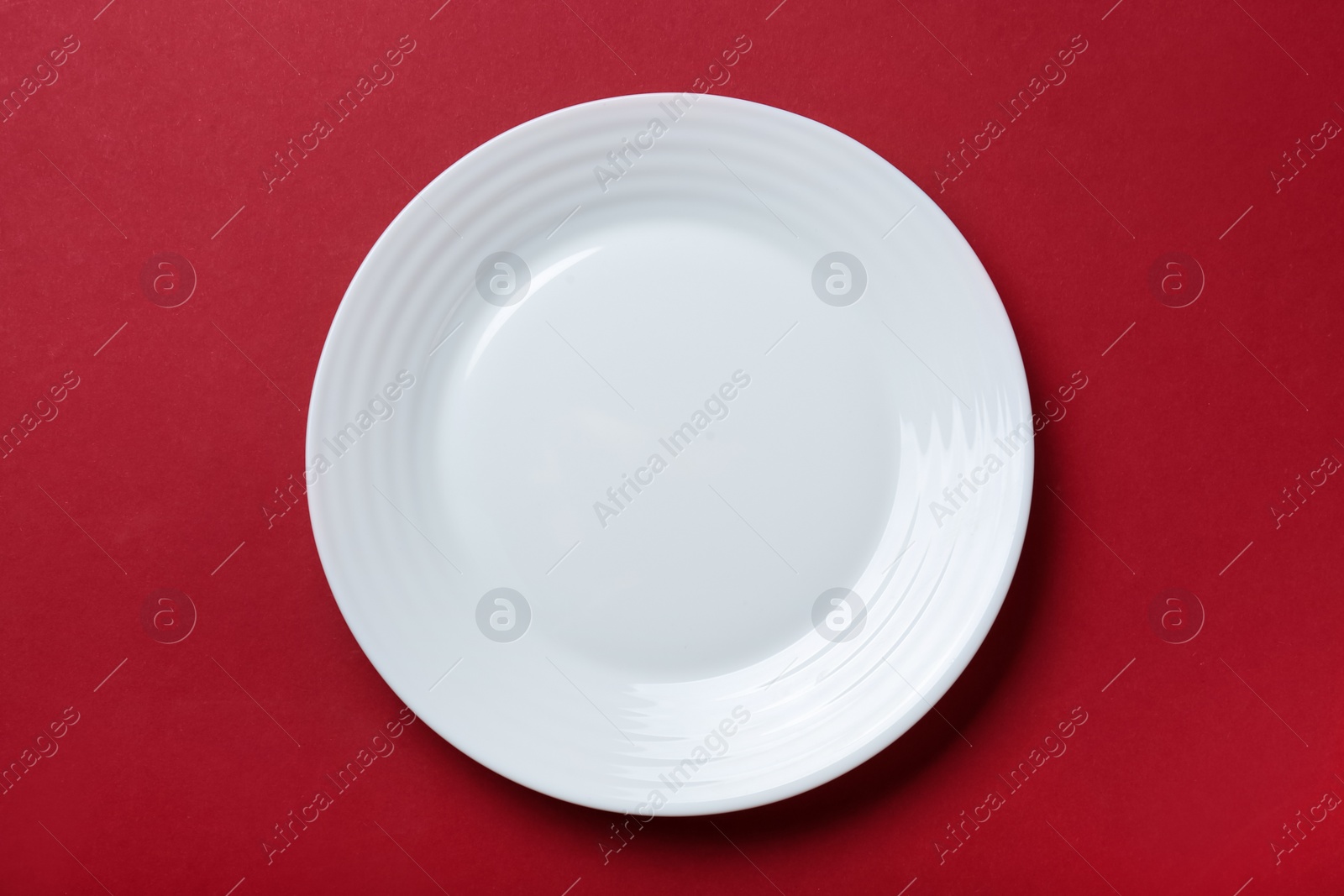 Photo of Empty white ceramic plate on red background, top view