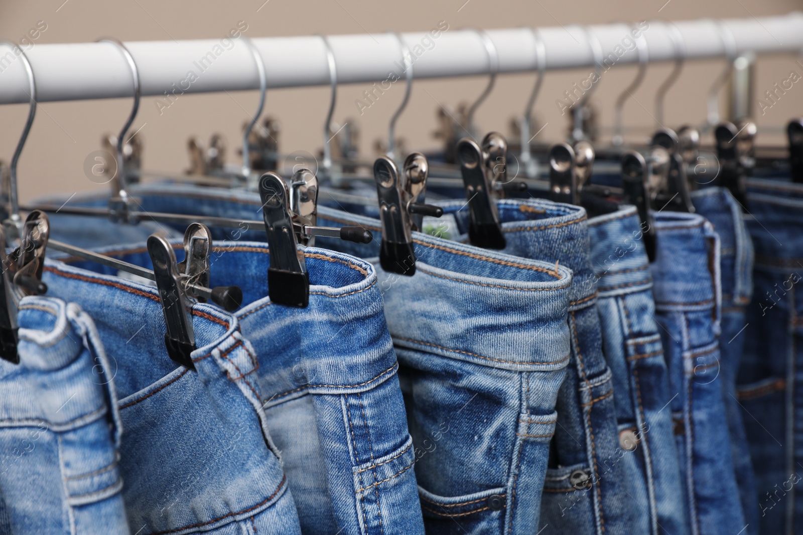 Photo of Rack with stylish jeans on beige background, closeup