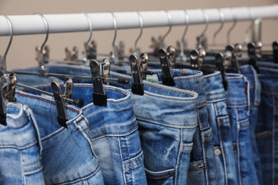 Rack with stylish jeans on beige background, closeup