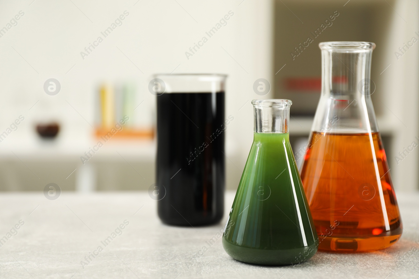 Photo of Flasks and beaker with different types of crude oil on light grey table, space for text