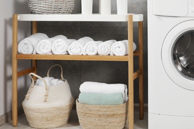 Photo of Wooden shelf and wicker baskets with soft terry towels in bathroom