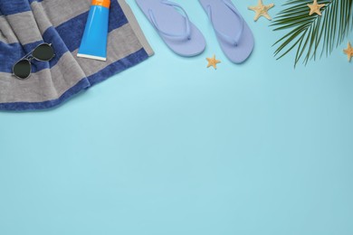 Photo of Beach towel, flip flops, sunglasses and sun protection product on light blue background, flat lay. Space for text