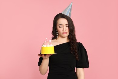 Photo of Coming of age party - 21st birthday. Upset woman holding delicious cake with number shaped candles on pink background