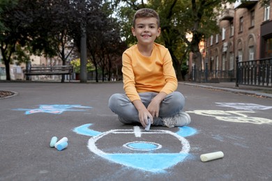 Child drawing rocket with chalk on asphalt