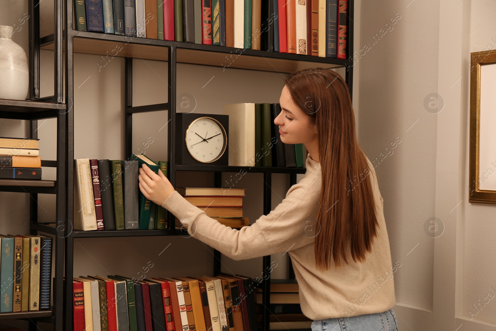 Photo of Young woman choosing book on shelf in home library
