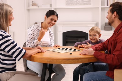 Photo of Family playing checkers at wooden table in room. Mother enjoying winning