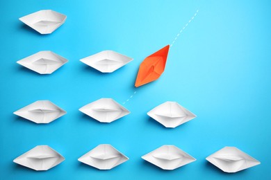Photo of Orange paper boat floating away from others on light blue background, flat lay. Uniqueness concept