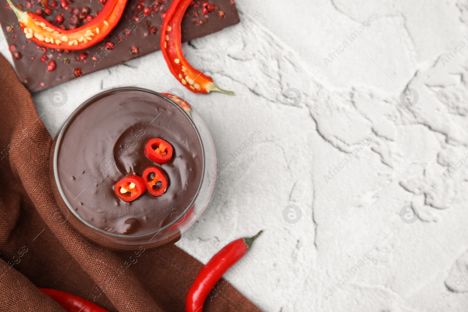 Photo of Glass of hot chocolate with chili pepper on white textured table, flat lay. Space for text