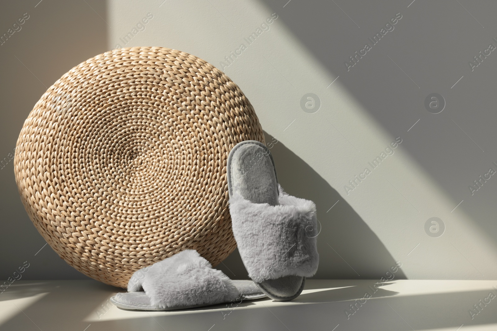 Photo of Pair of soft slippers and wicker pouf on floor near white wall, space for text