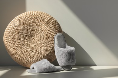 Photo of Pair of soft slippers and wicker pouf on floor near white wall, space for text