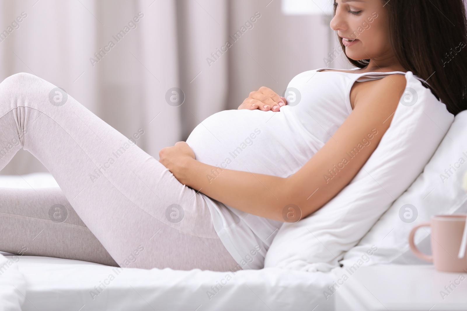 Photo of Happy pregnant woman lying on bed at home, closeup