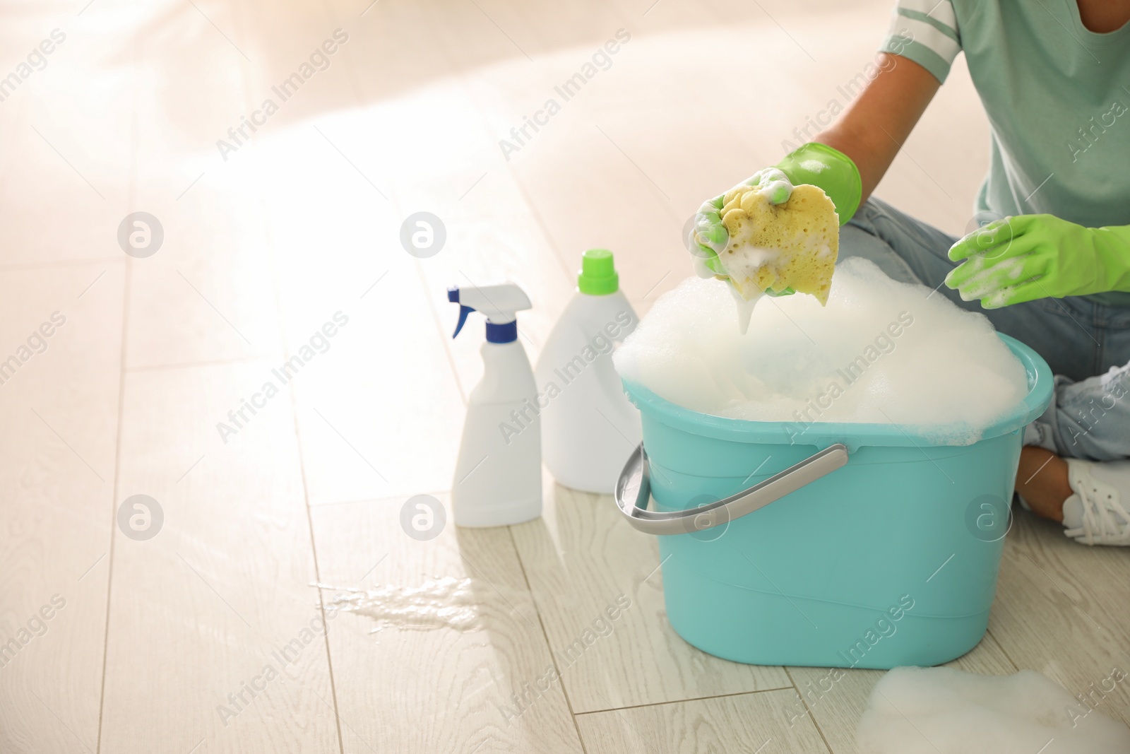 Photo of Woman holding sponge with foam over bucket indoors, closeup. Cleaning supplies