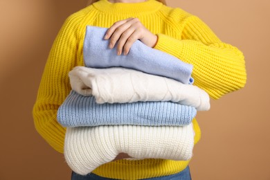 Photo of Woman with stack of casual sweaters on light brown background, closeup