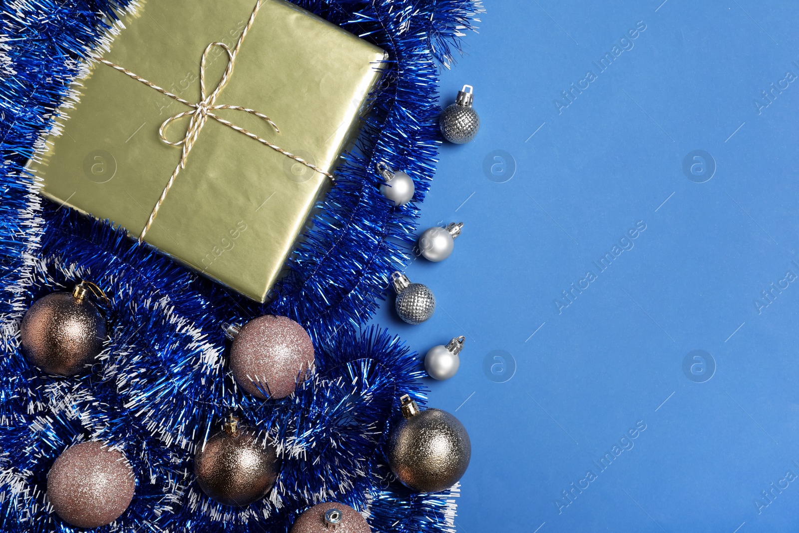 Photo of Bright tinsel, Christmas balls and gift box on blue background, flat lay. Space for text