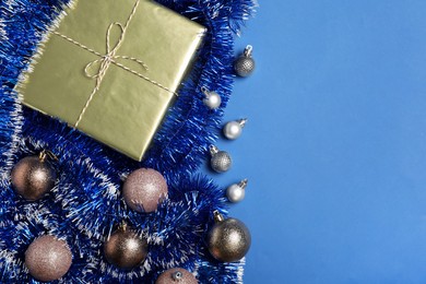 Photo of Bright tinsel, Christmas balls and gift box on blue background, flat lay. Space for text