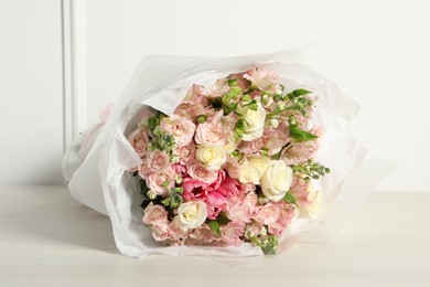 Photo of Beautiful bouquet of fresh flowers on wooden table near white wall