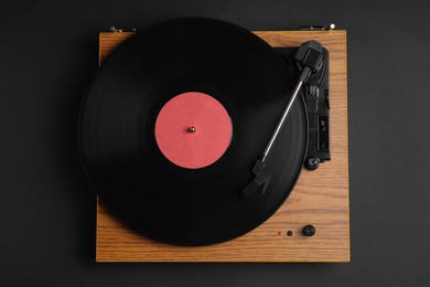 Photo of Modern vinyl record player with disc on black background, top view