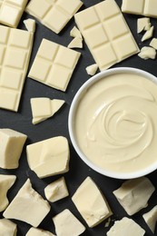 Photo of Tasty white chocolate paste in bowl and pieces on black table, flat lay