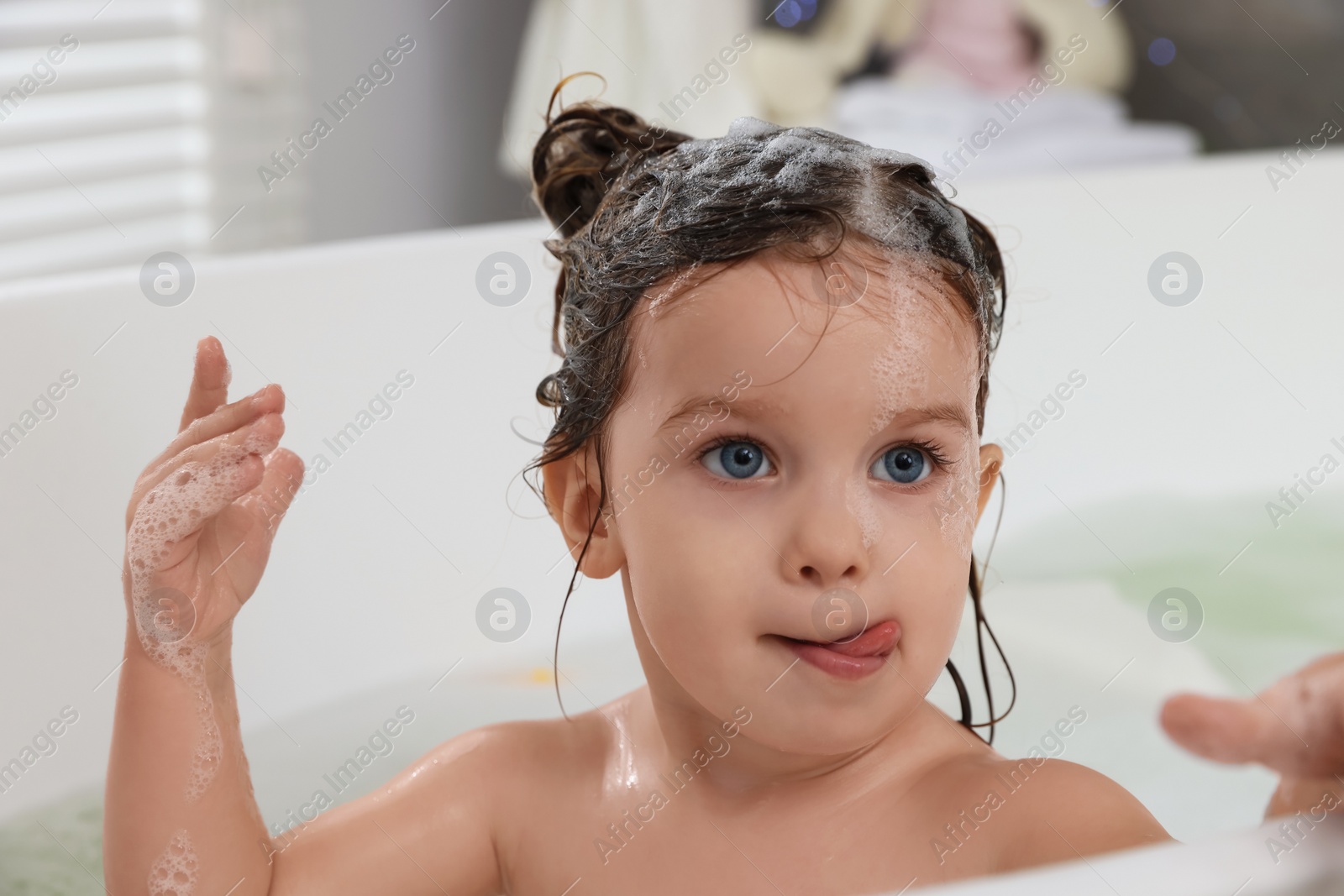 Photo of Cute little girl washing hair with shampoo in bathroom