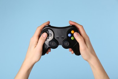 Woman using game controller on light blue background, closeup