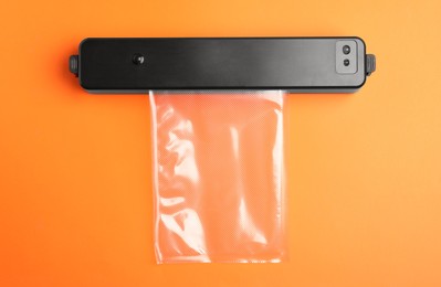 Photo of Sealer for vacuum packing with plastic bag on orange background, flat lay