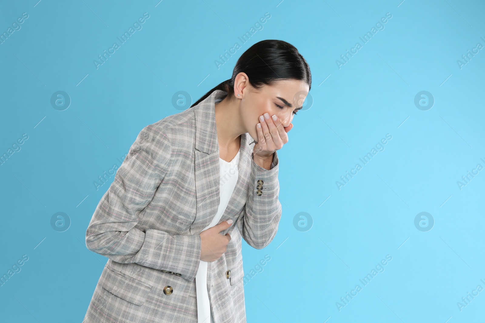Photo of Woman in office suit suffering from stomach ache and nausea on light blue background, space for text. Food poisoning
