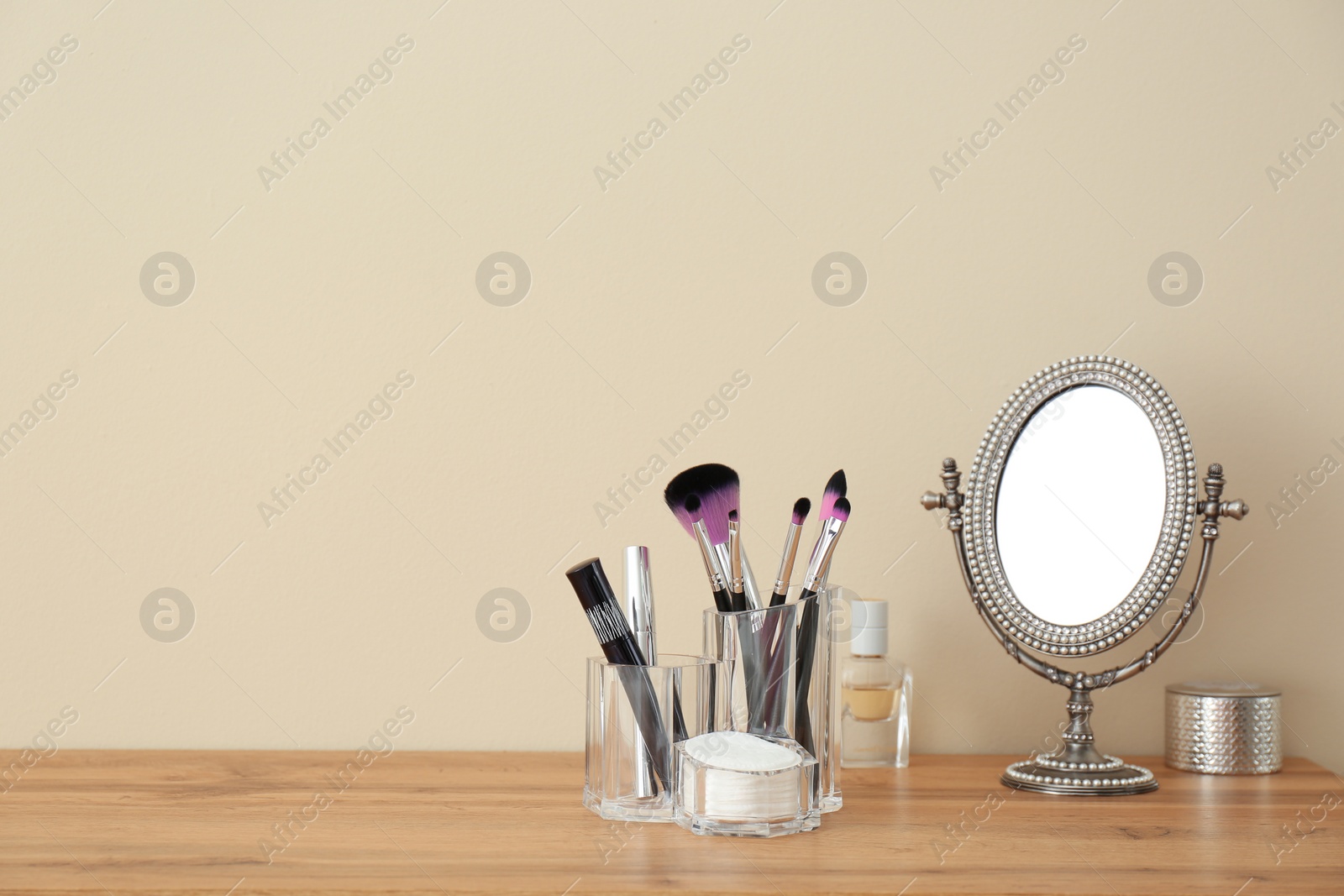 Photo of Organizer with makeup cosmetic products and mirror on table against light wall. Space for text