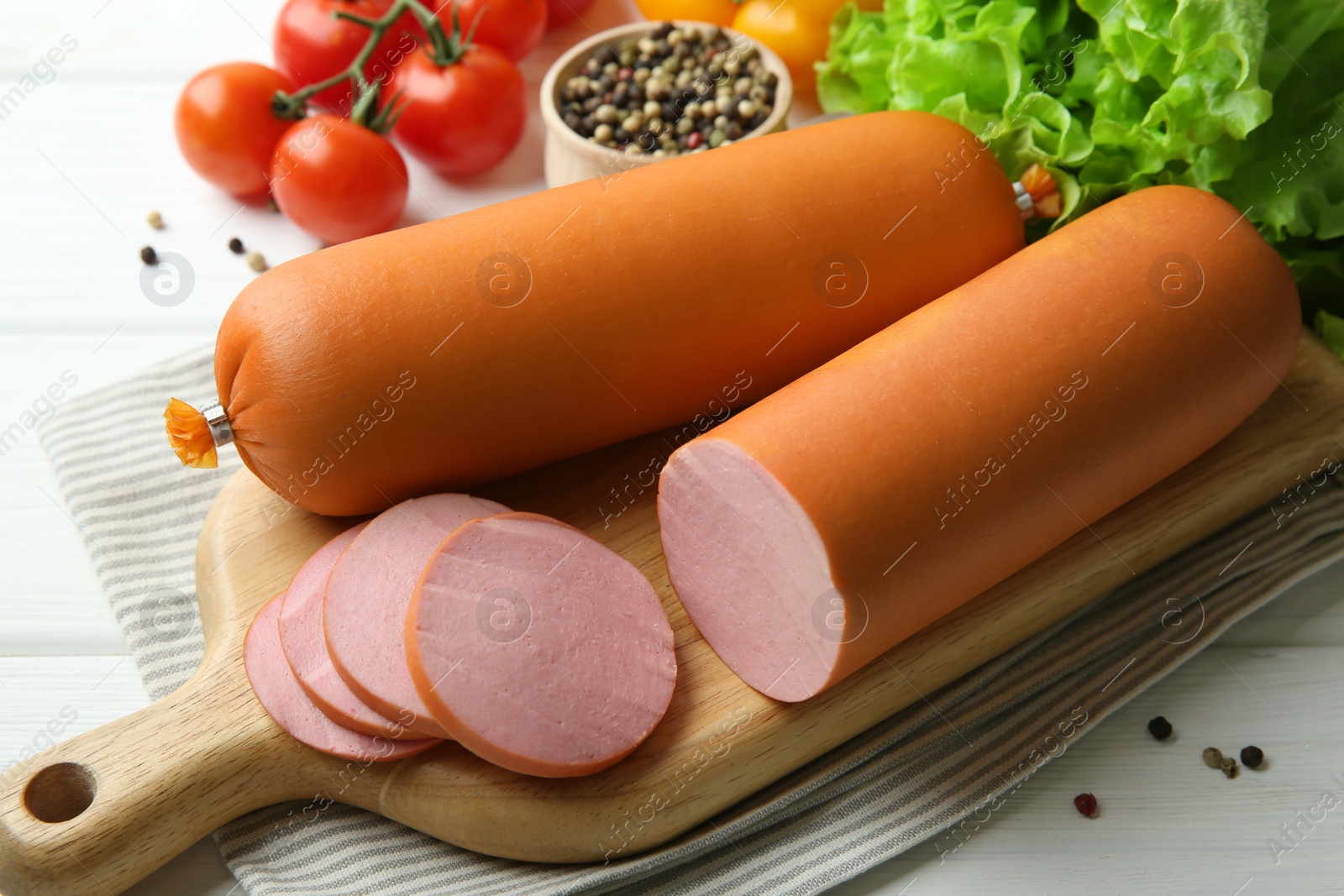 Photo of Board with tasty boiled sausages and products on white wooden table