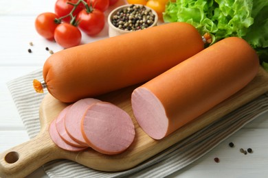 Photo of Board with tasty boiled sausages and products on white wooden table