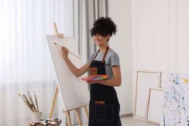 Photo of Young woman painting on easel with canvas in studio