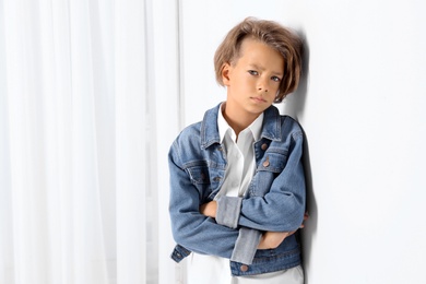 Photo of Cute little boy in casual outfit near white wall in room. Space for text