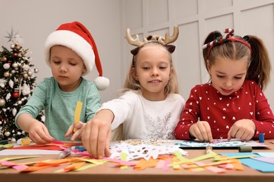 Cute little children making Christmas cards at table in decorated room