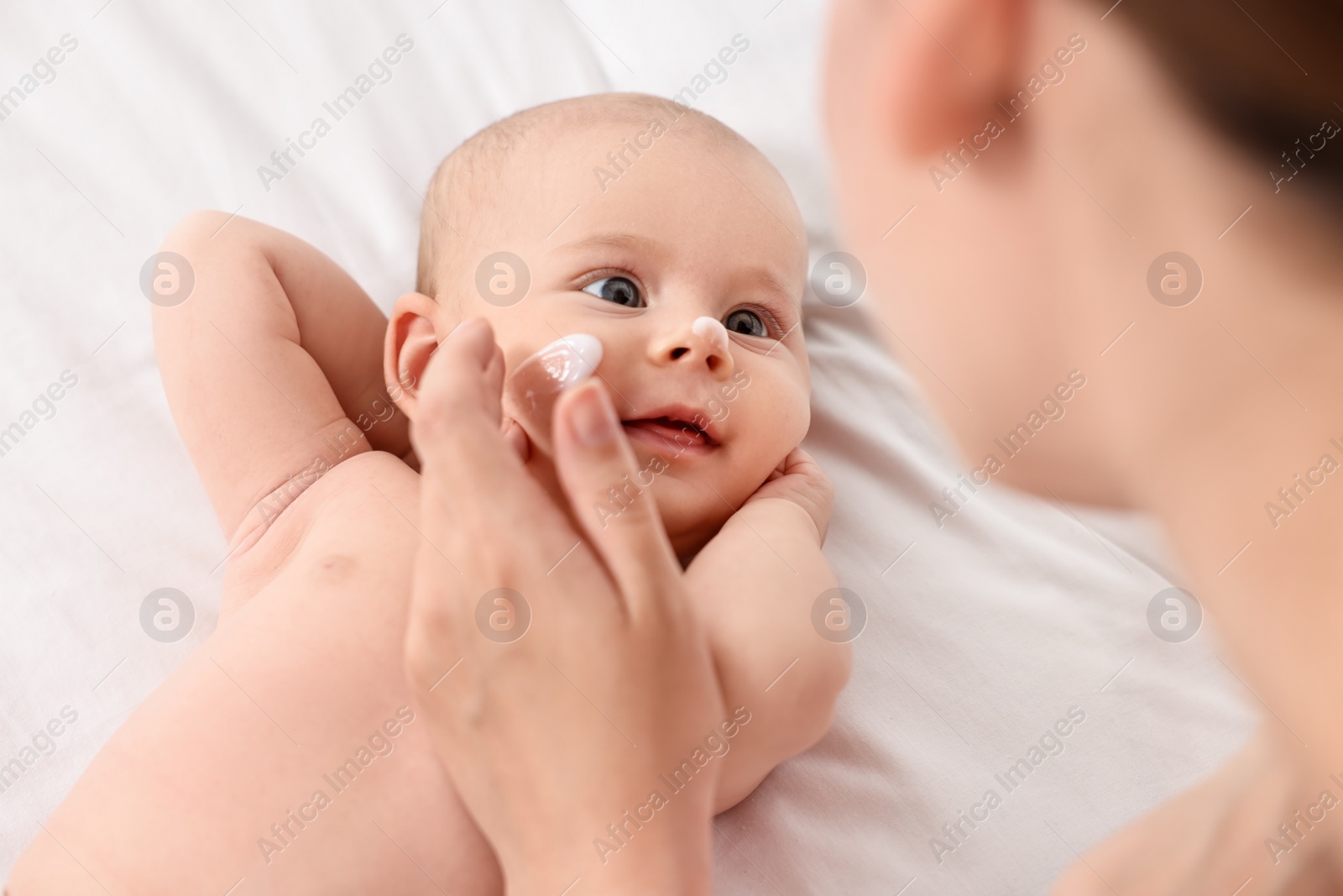 Photo of Woman applying cream onto baby`s face on bed, closeup