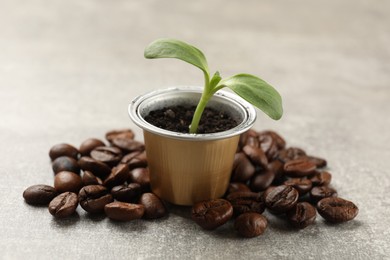 Photo of Coffee capsule with seedling and beans on light grey table, closeup