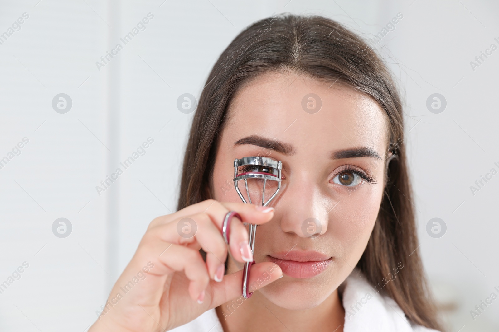 Photo of Attractive young woman with eyelash curler indoors