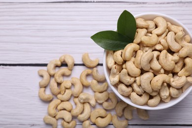 Photo of Tasty cashew nuts and green leaves on white wooden table, top view