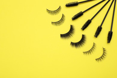 Photo of Fake eyelashes and brushes on yellow background. Space for text