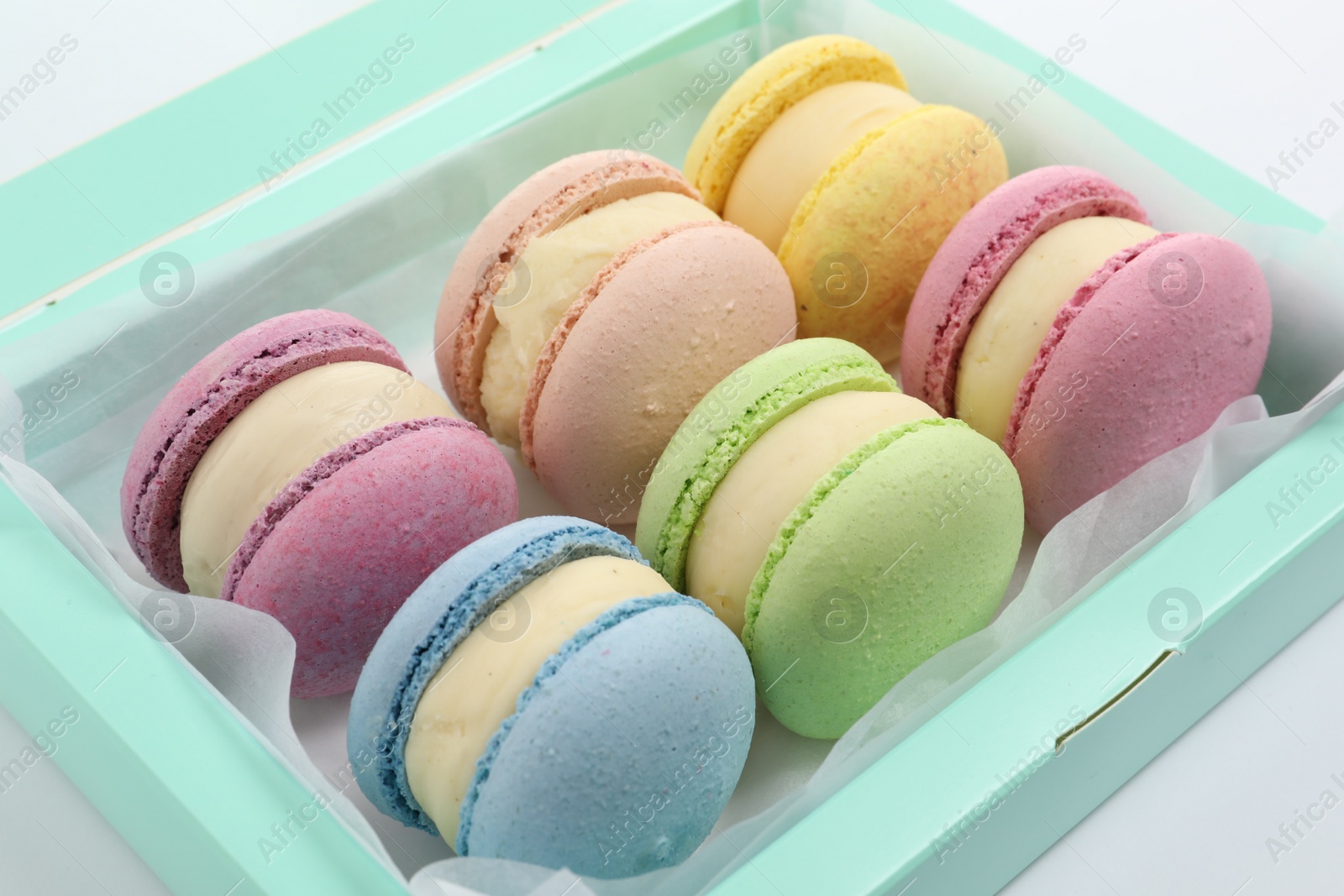 Photo of Many delicious colorful macarons in box on white background, closeup 